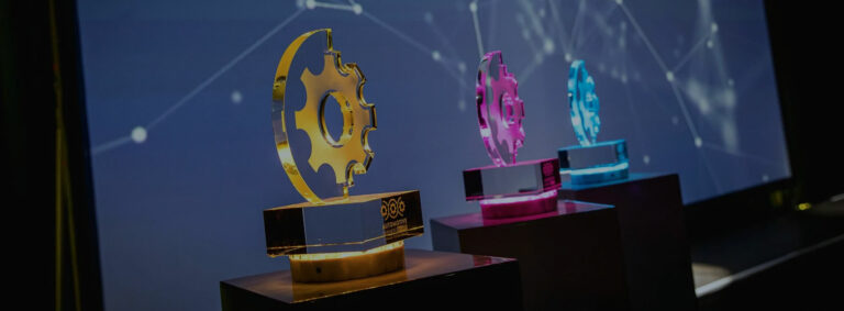 Automotiv Business Award – 3 Preise in Form eines Zahnrades in gelb, pink und blau stehen auf einer Bühne.